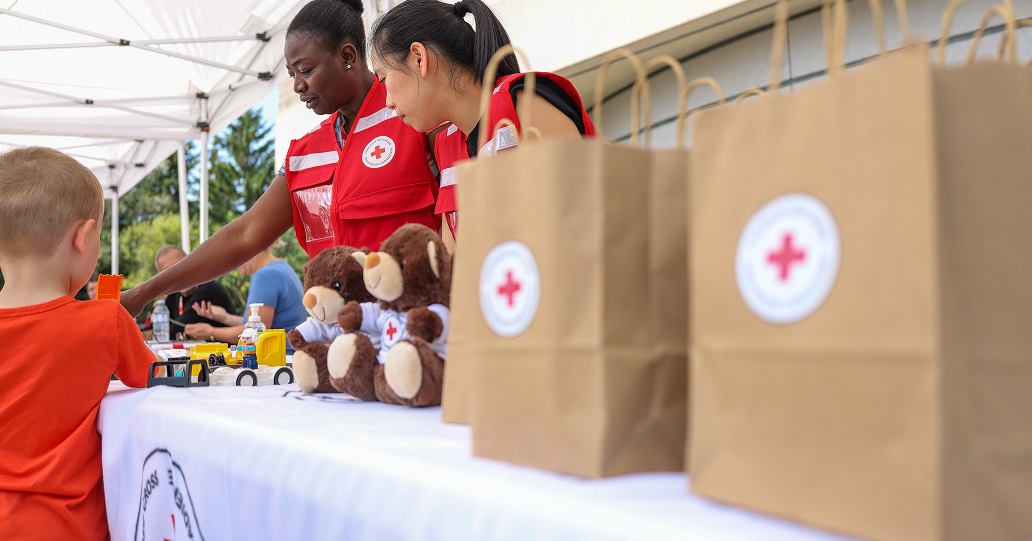 Two Canadian Red Cross volunteers distribute  bags with Red Cross teddy bears to children