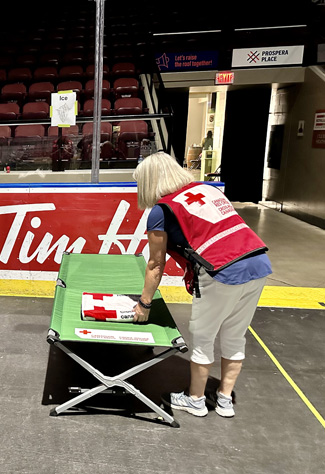 Two people wearing Red Cross vests set up emergency beds for wildfire evacuees