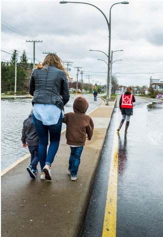 A woman and two children walk on a wet sidewalk, during flooding from heavy rain and snowmelt.