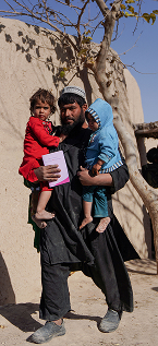 A man carries two children in his arms as he walks away from a building 
