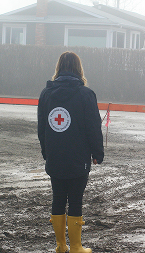 A person in a CRC coat stands in the middle of a road, surrounded by floodwaters, highlighting the disaster's impact. 