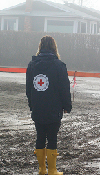 Une personne portant un manteau du CRC se tient au milieu d'une route, entourée par les eaux de crue, soulignant l'ampleur du sinistre. 