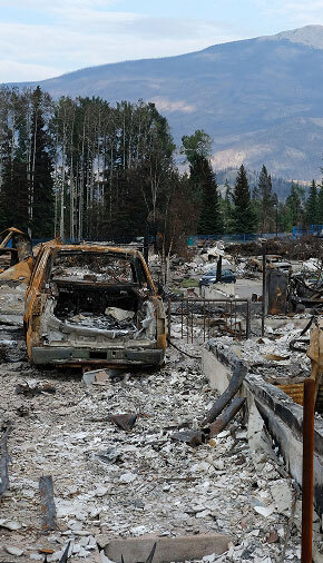 A burned building with mountains in the background, highlighting the devastation from the Jasper Wildfire 