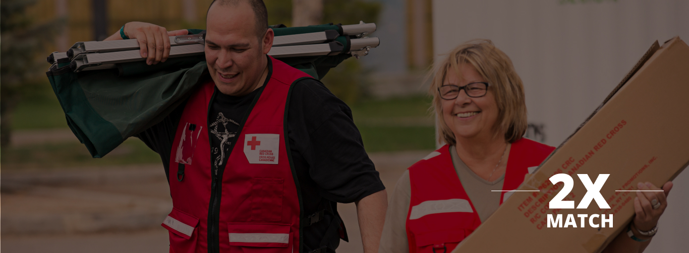 Two Canadian Red Cross volunteers smile as they both carry large supplies.