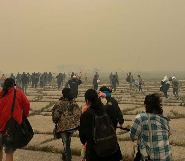 Des évacués marchant vers le hangar de l'aéroport, à peine visible à cause de la fumée dans l'air.