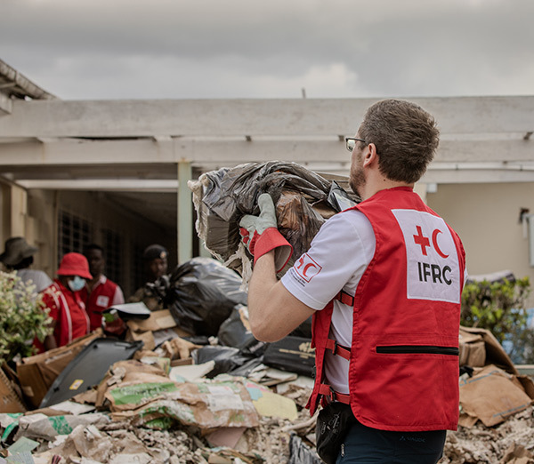 Un homme en gilet rouge porte un grand sac de débris, aidant au nettoyage après l'ouragan Mélissa.