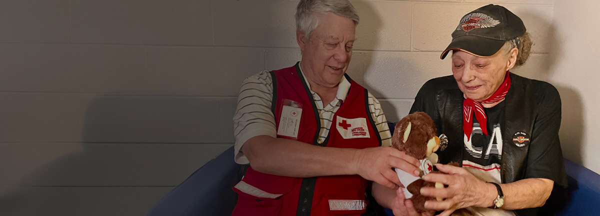 A Canadian Red Cross volunteer hands a teddy bear to an elderly person