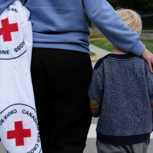 A Canadian Red Cross volunteer walking beside a small child.