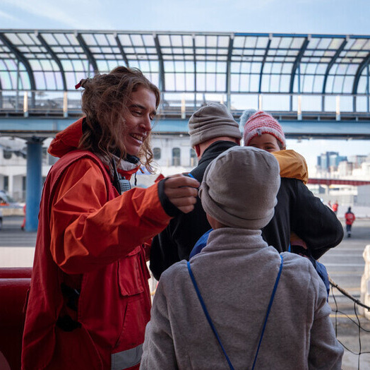 A woman in a red Canadian Red Cross jacket, helps a child.