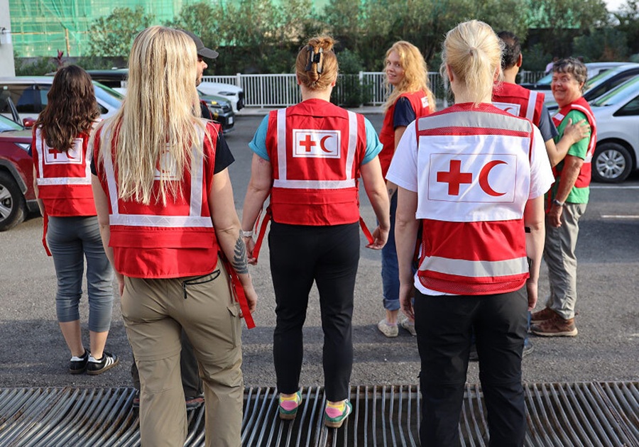 A group of smiling International Federation of Red Cross and Red Crescent Societies staff wearing red vests walk together through a parking lot.