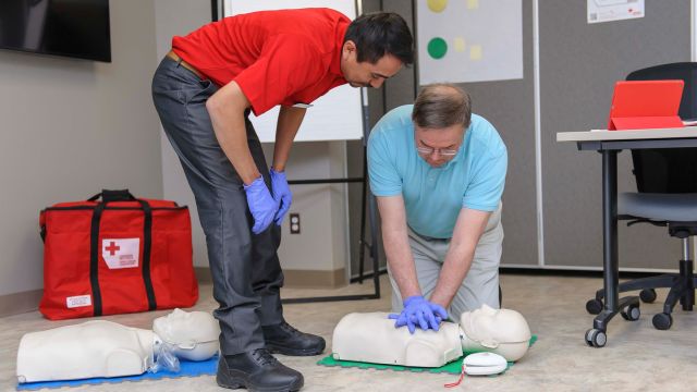 Two people standing over a mannequin, one person demonstrating how to perform CPR