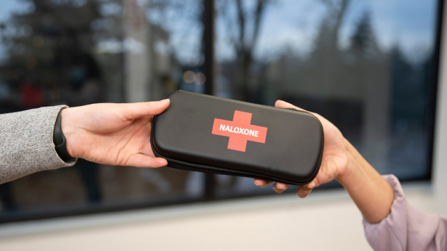 The hands of a person handing a naloxone kit to another person.