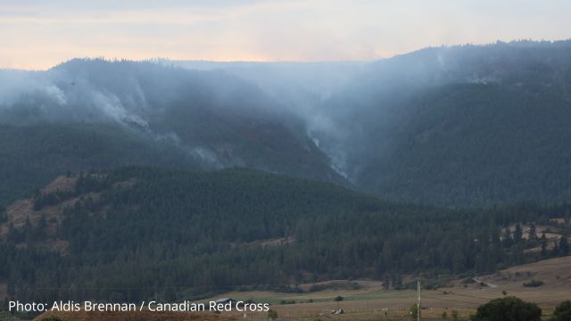 Wildfire smoke covering a landscape photo of mountains and trees.