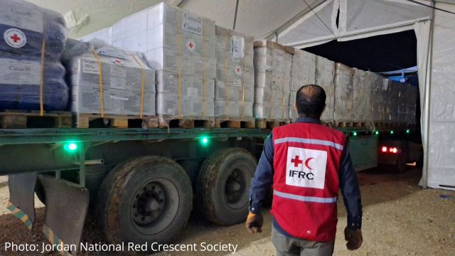 An IFRC personnel stands in front of a trailer with humanitarian supplies
