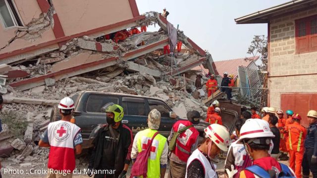 Des premiers répondants de la Croix-Rouge du Myanmar se tiennent devant un immeuble effondré.