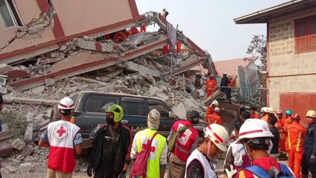 Des premiers répondants de la Croix-Rouge du Myanmar se tiennent devant un immeuble effondré.