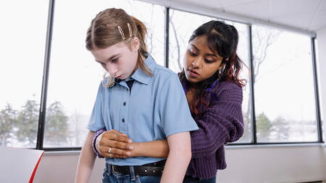 Person performing abdominal thrusts on a child. The adult stands behind the child, wrapping their arms around the child's waist
