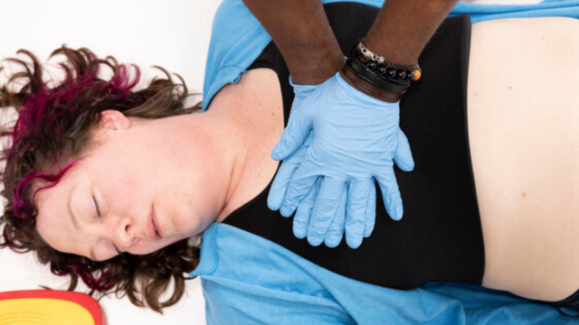 A person performing chest compressions on another individual lying on the ground, providing CPR