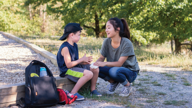 Une adulte applique un bandage sur le genou d’un enfant ayant besoin des premiers soins en plein air.
