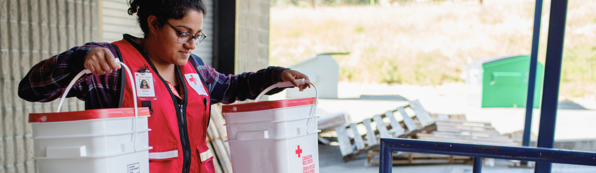 A Red Cross volunteer holds two buckets up.