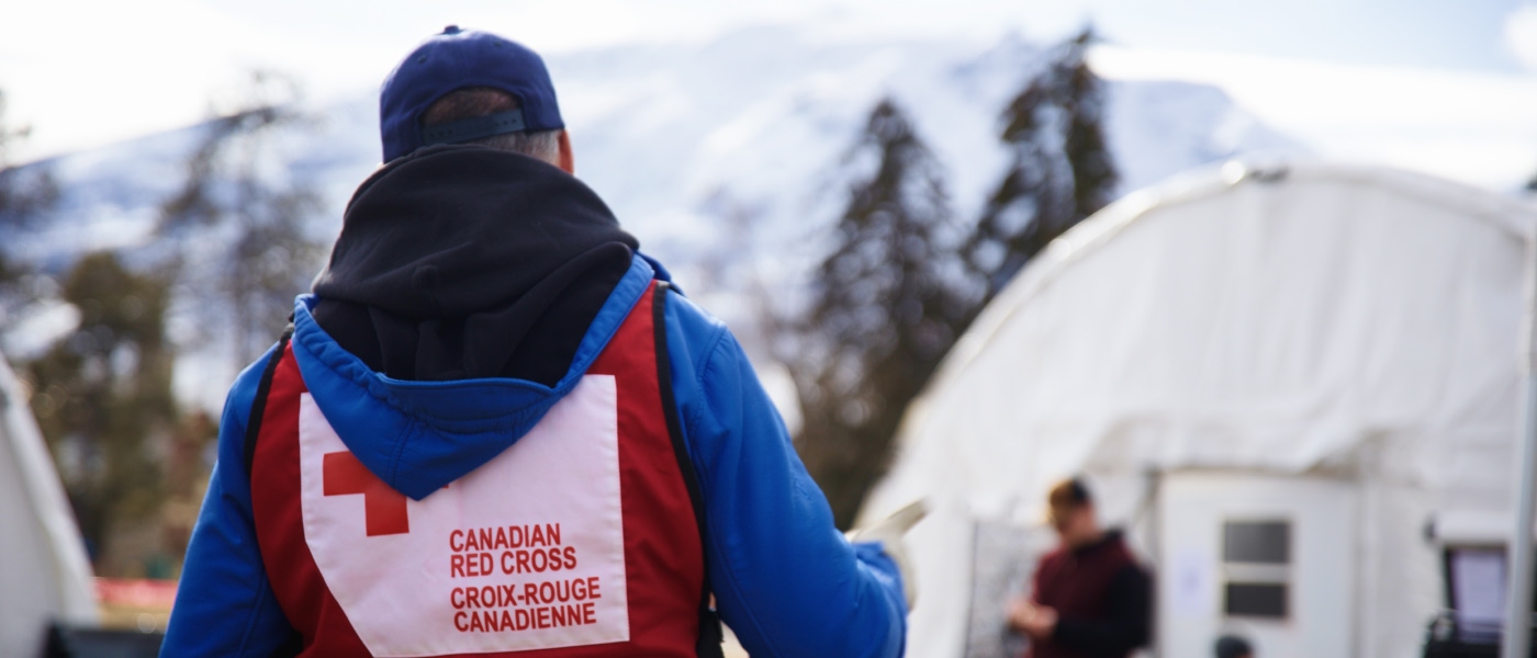 Un homme portant un gilet de la Croix-Rouge par-dessus une veste bleue se tient prêt à aider dans une mission humanitaire.