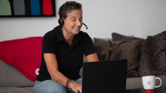 A person smiling while working on a computer, sitting on a sofa.