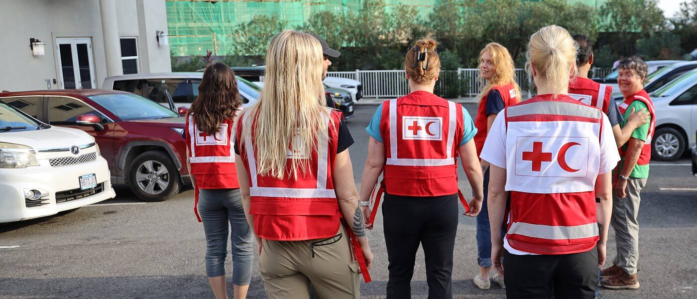 Un groupe de membres souriants du personnel de la Fédération internationale de la Croix-Rouge et du Croissant-Rouge, vêtus de gilets rouges, traversent ensemble un parking.