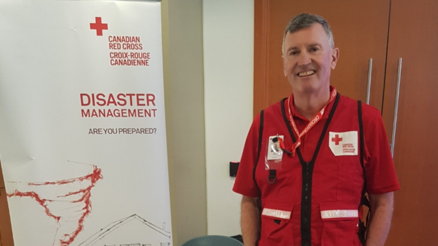 Un bénévole de la Croix-Rouge canadienne debout à côté d'une affiche sur la gestion des catastrophes