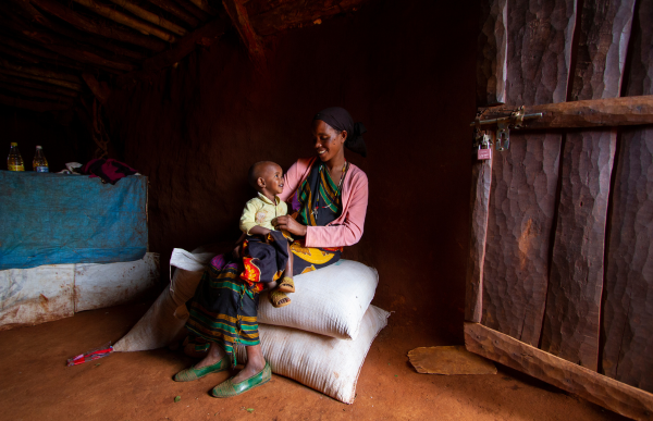 A woman in colourful clothing sitting while holding her baby in her lap.