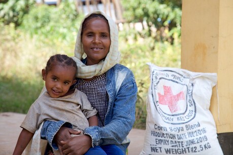 A woman wearing a head scarf smiling while holding a smiling child