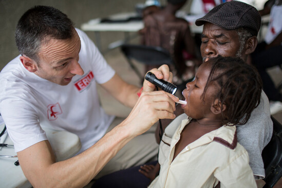 A child receiving a throat exam from a Red Cross doctor