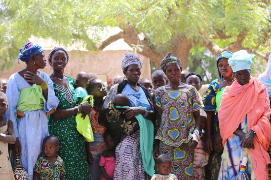 A group of women and their children standing together in front of a large tree.