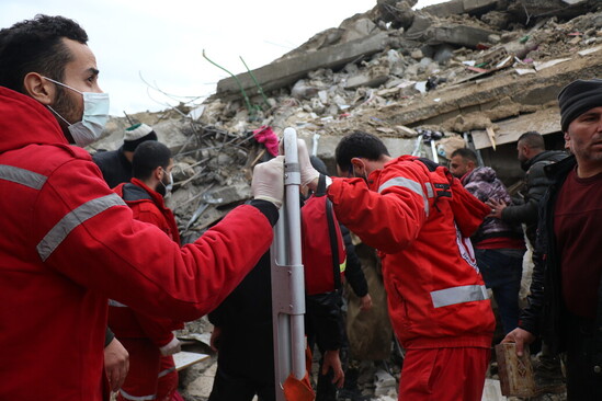 A group of people in red uniforms working in front of a destruction site