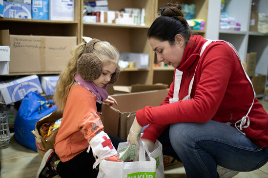 Woman in red shirt packing a donation bag with a young girl