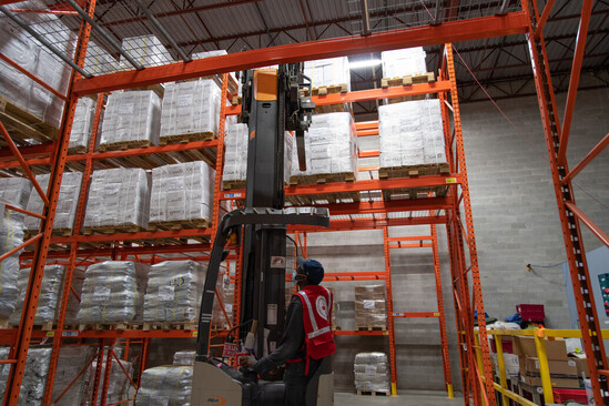 Person in Red Cross vest operating machinery to stock warehouse shelves