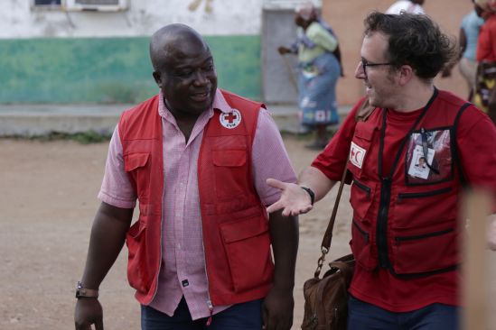 Two Red Cross personnel wearing Red Cross vests walk while talking