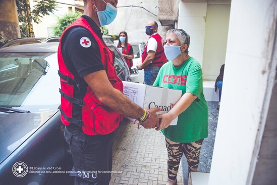 Man in a Red Cross vest gives woman a box with the Government of Canada logo