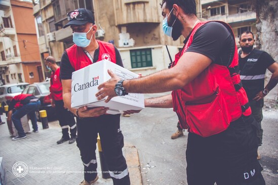 Two men in red vests holding up a white box with the Government of Canada logo