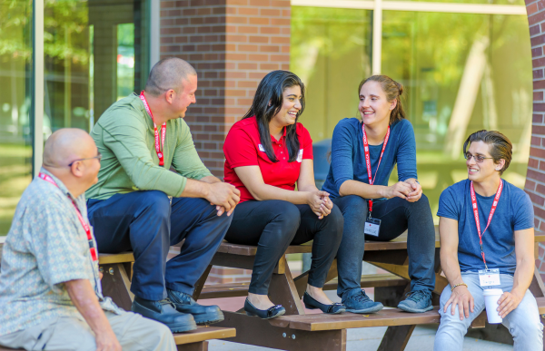 A group of people are gathered outside a building, chatting and enjoying each other's company. Each person is wearing a Red Cross identification.