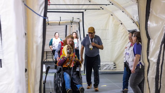 Une femme pousse une personne en fauteuil roulant, entourée d'autres, dans un hôpital mobile.