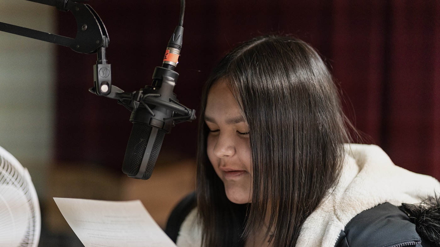 A young woman reads a script into a microphone.