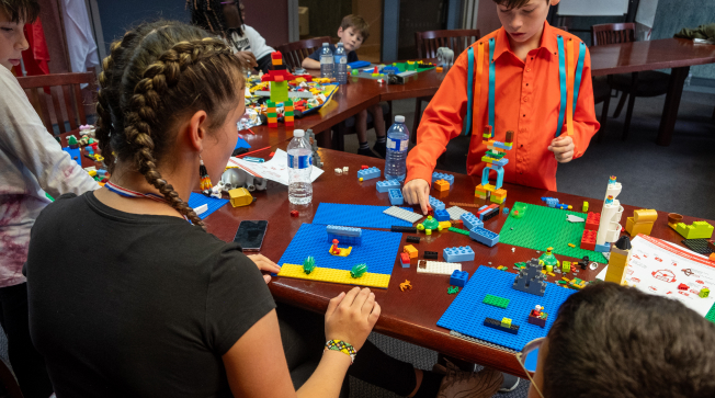 Quatre enfants jouent avec des blocs LEGO. Un jeune garçon porte une chemise à rubans.