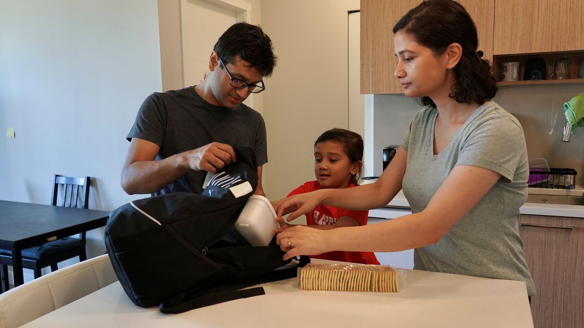 A man, woman, and child pack a Grab and Go bag. There is a bag of crackers on the table beside them.