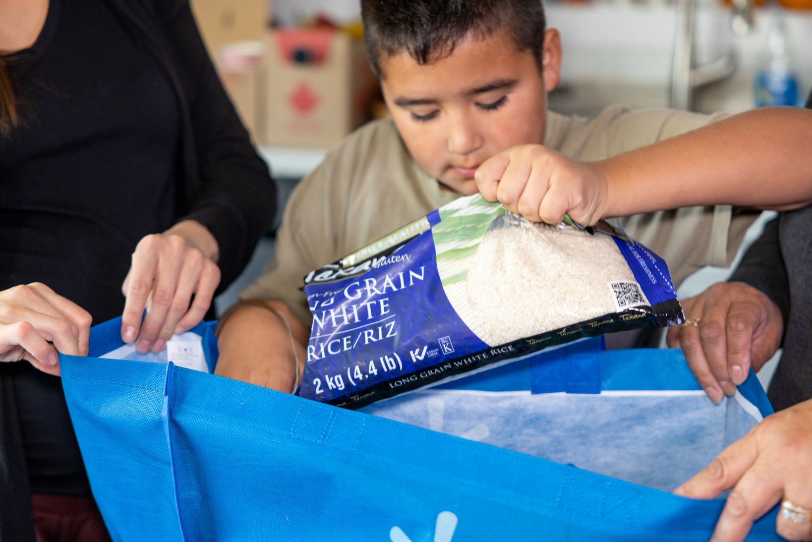  A child puts a bag of rice into a reuseable bag while packing an emergency kit with his family.