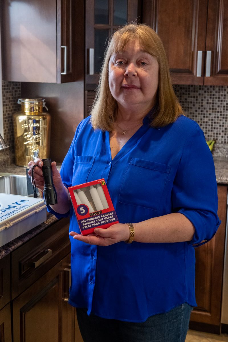 A woman in a blue shirt displays some of her emergency supplies. She holds candles and a flashlight. 