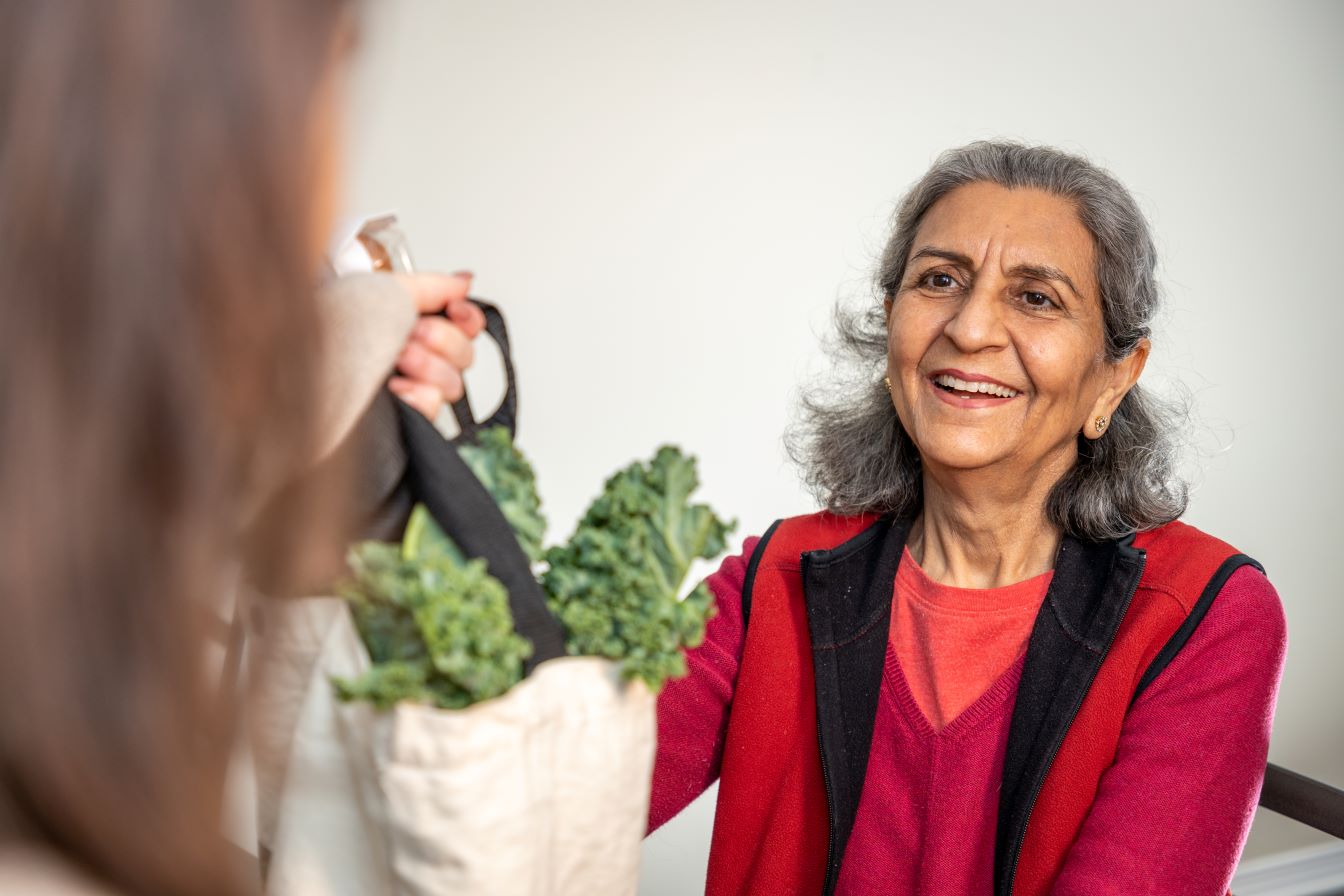 A person hands a bag of groceries to an older woman.