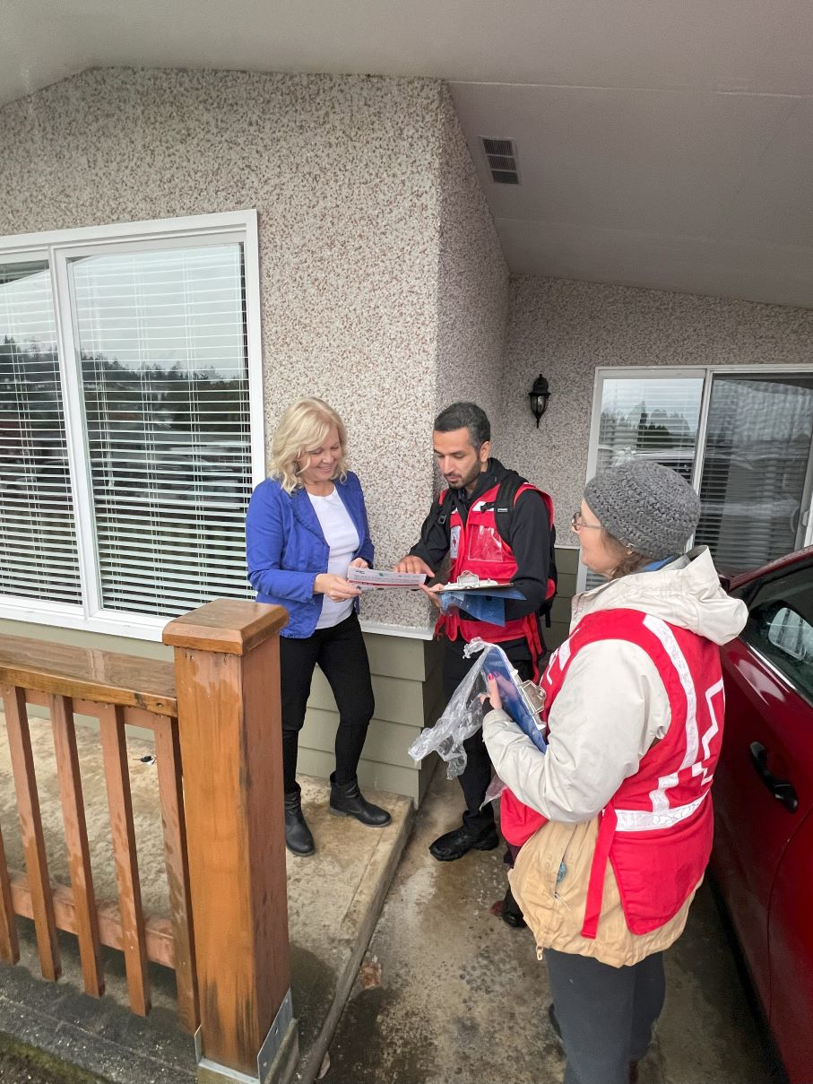 Two people in Red Cross vests show a woman information at her door.