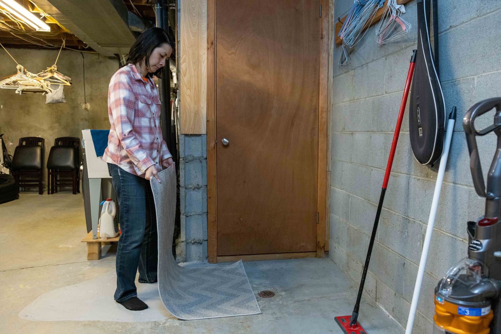 A woman removes a rug that was covering a drain in a basement. (Credit John Falcon)