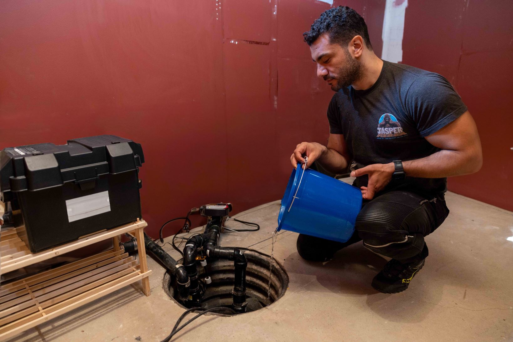 A man pours water from a bucket into a sump pump. (Credit John Falcon)