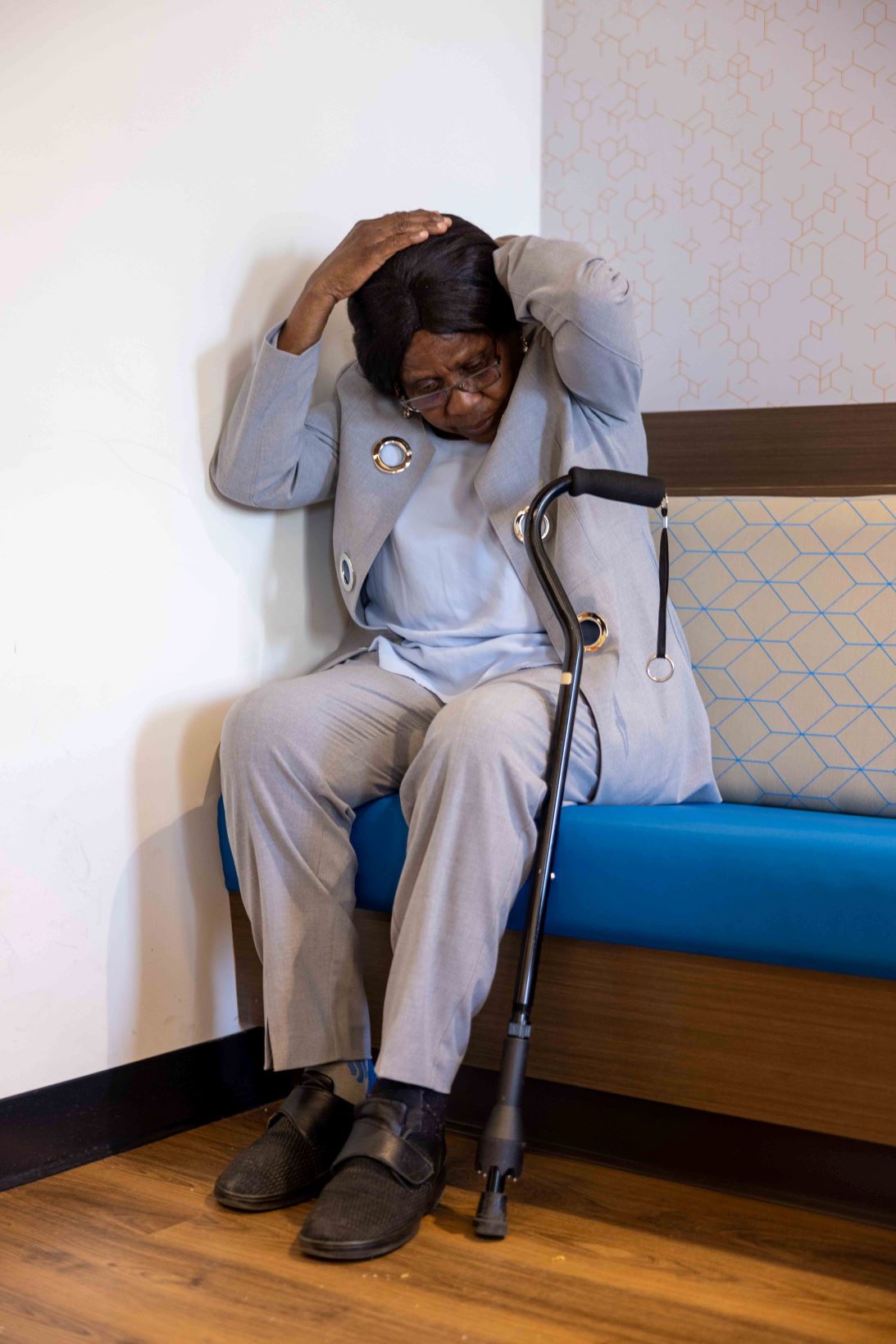 An older person sits in the corner covering her head; her cane is beside her. (Credit John Falcon)